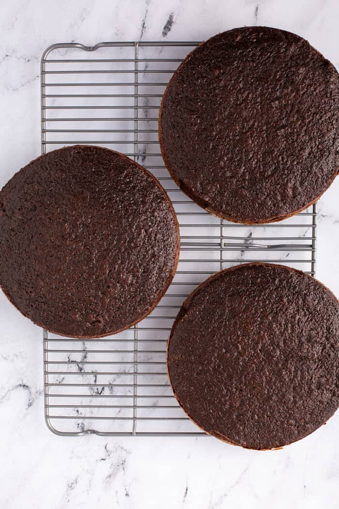 Overhead view of 3 layers of baked Hershey's chocolate cake cooling on a wire rack on a marble counter