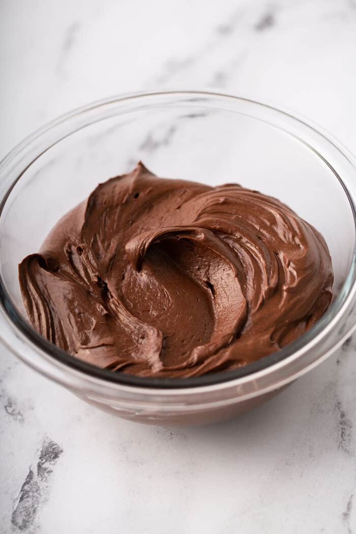 Homemade chocolate frosting in a glass mixing bowl on a marble counter