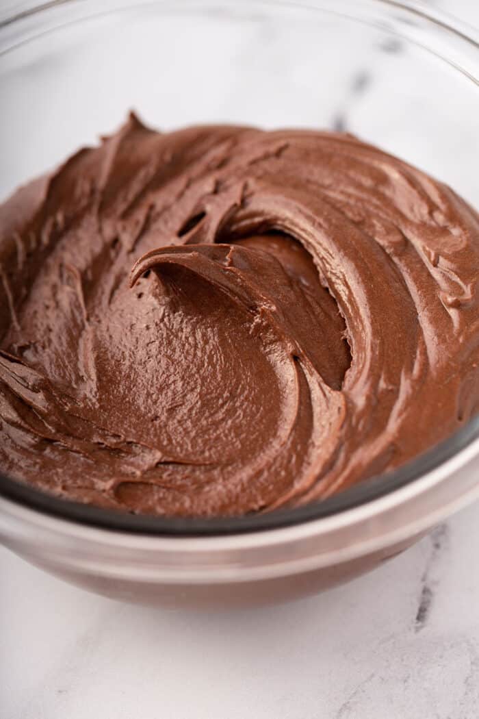 Close up of homemade chocolate frosting in a glass bowl on a marble counter