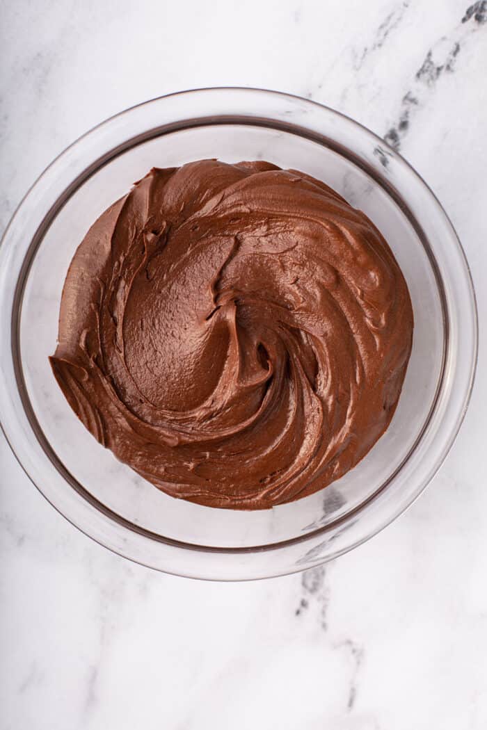 Overhead view of homemade chocolate frosting in a glass mixing bowl on a marble counter