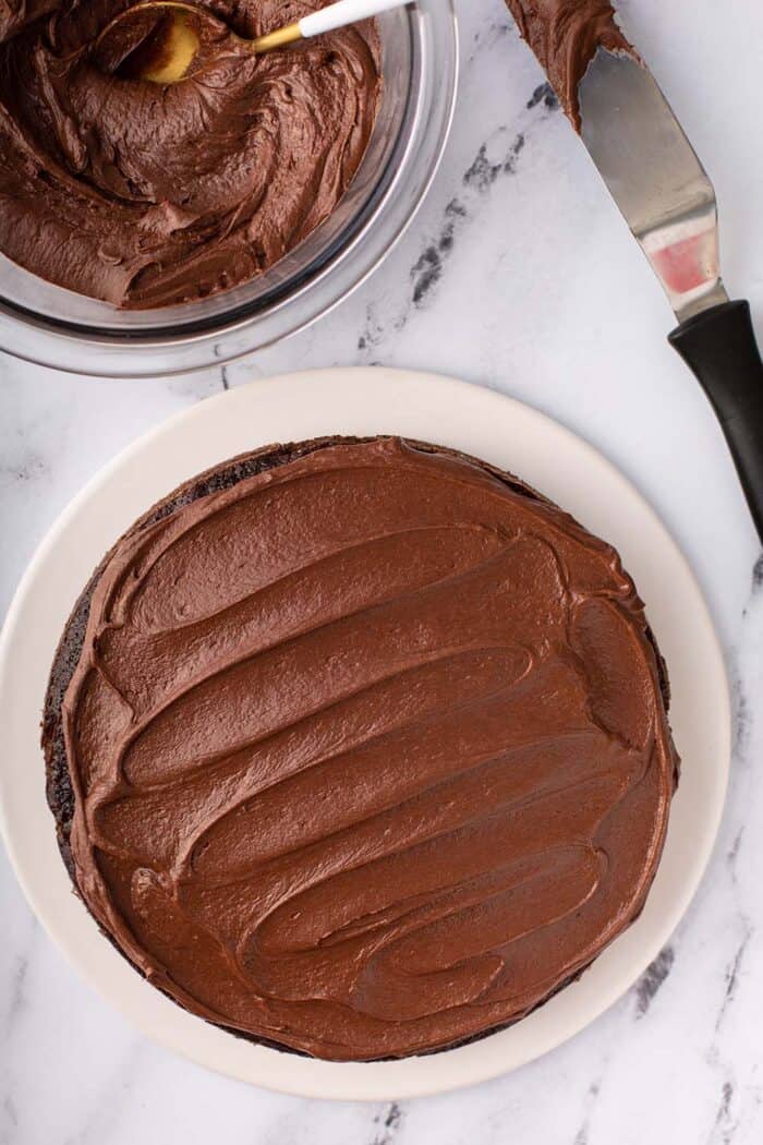 Overhead view of an offset spatula frosting a layer of Hershey's Chocolate Cake with homemade chocolate frosting