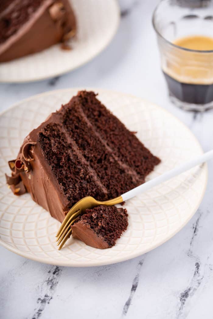 Close up view of slice of Hershey's chocolate cake on a white plate with a fork cutting off a corner of the cake