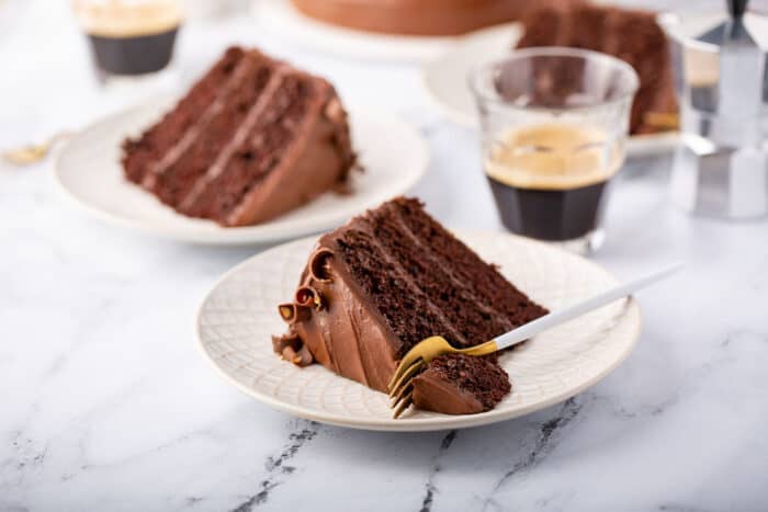 Slice of 3-layer Hershey's chocolate cake on a white plate with a fork cutting off a corner