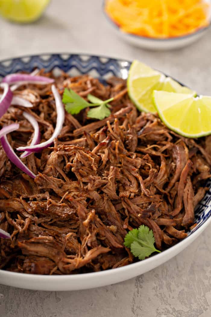 Close up of Chipotle barbacoa in a blue and white bowl topped with lime wedges, red onion and cilantro