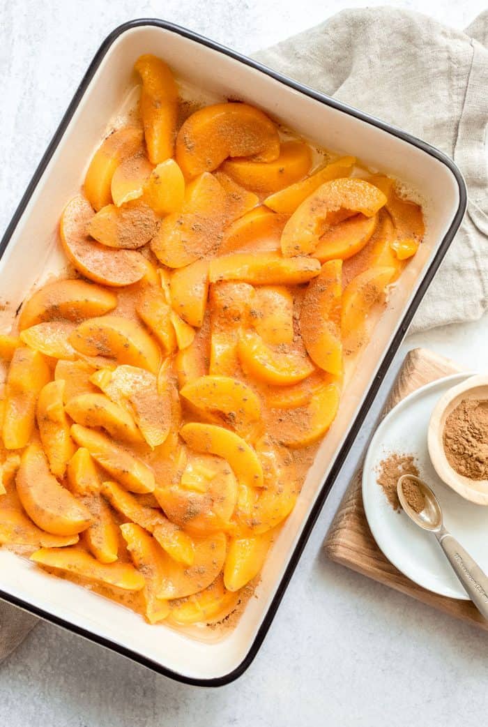 Canned peaches sprinkled with cinnamon in a baking dish, ready to be made into peach cobbler