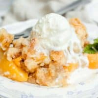 Serving of easy peach cobbler on a white plate with a scoop of vanilla ice cream melting on top of it