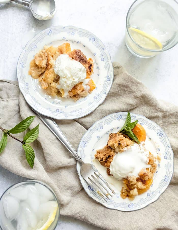 Two white plates each with a serving of easy peach cobbler topped with a scoop of vanilla ice cream