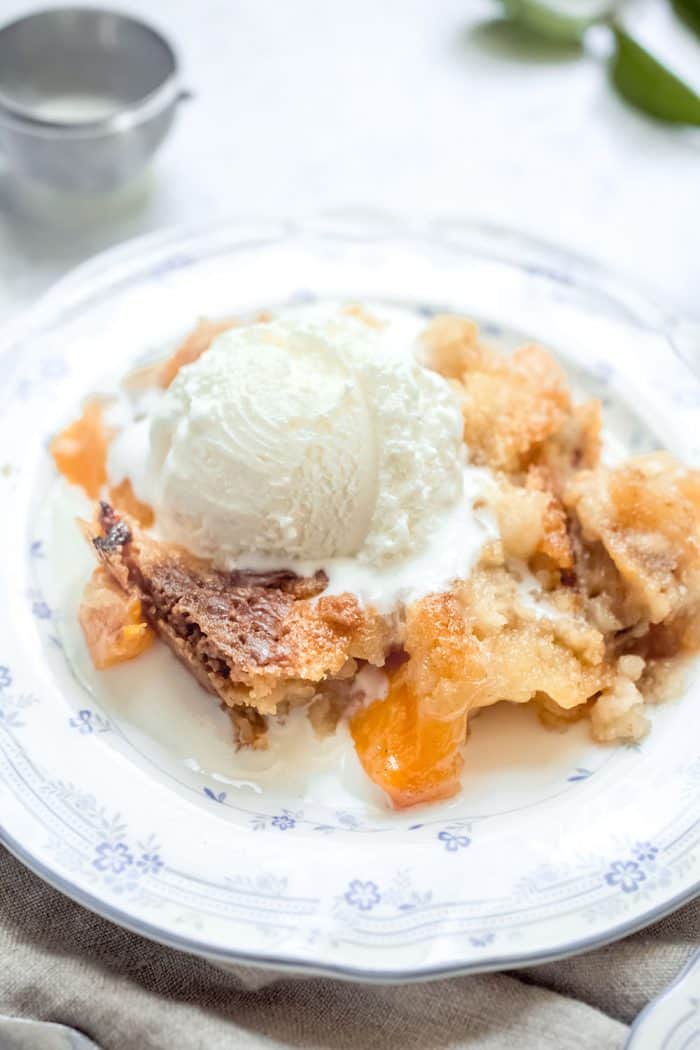 Peach cobbler on a white plate topped with a scoop of vanilla ice cream