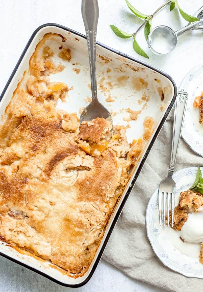 Baking pan of easy peach cobbler with a spoon in it, with several servings removed