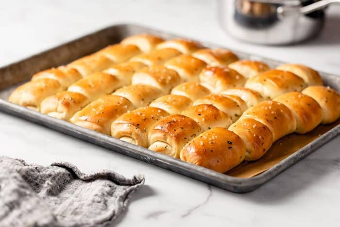 Baking sheet with freshly baked garlic and herb parker house rolls on a marble countertop