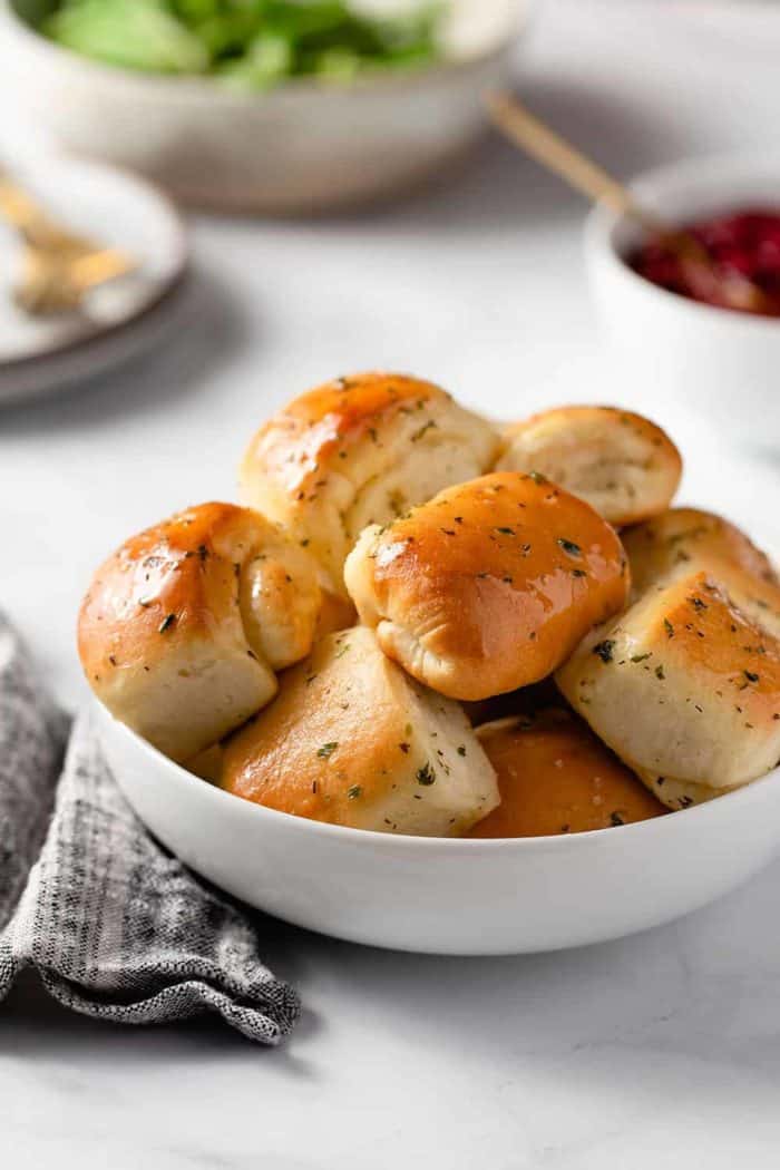 Close up of garlic and herb parker house rolls in a white bowl, set on a marble counter