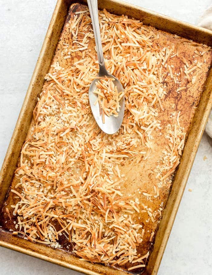 Toasted coconut on a sheet pan being tossed by a spoon