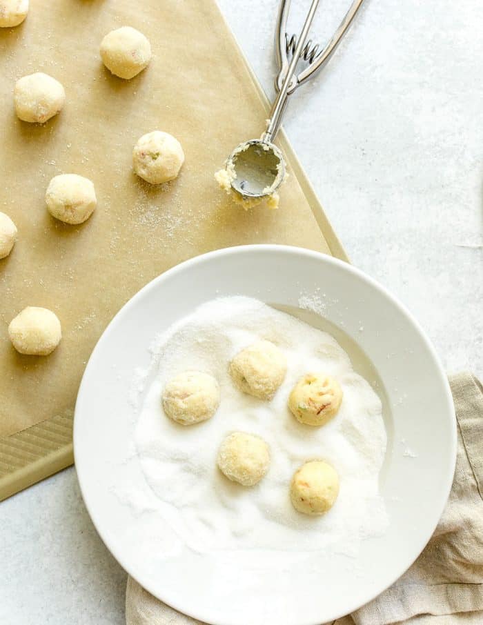 Lime sugar cookie dough balls being rolled in granulated sugar and placed on a parchment-lined sheet pan