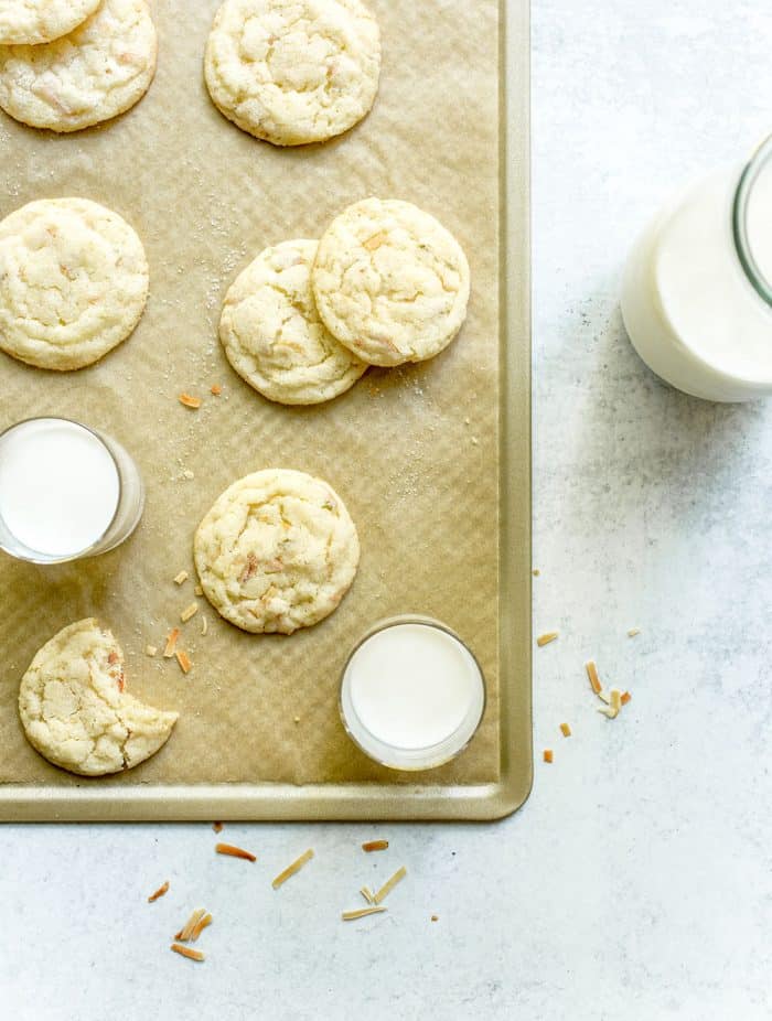 Glasses of milk and chewy lime sugar cookies scattered on a parchment-lined cookie sheet