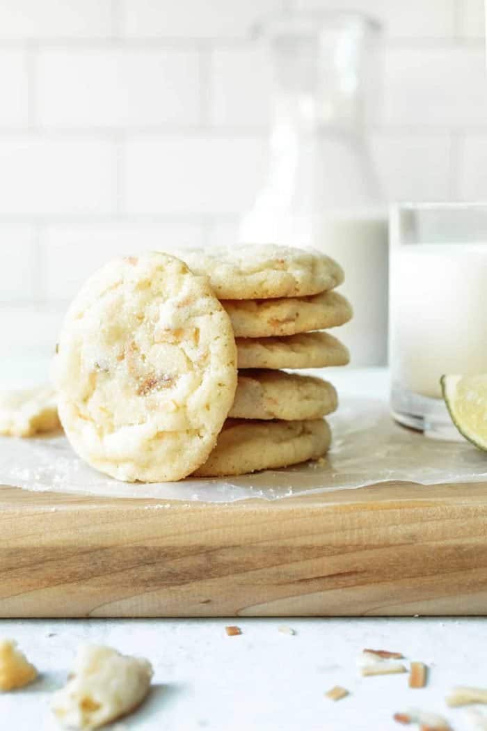 Chewy lime sugar cookies stacked on a parchment-covered cutting board next to a glass of milk