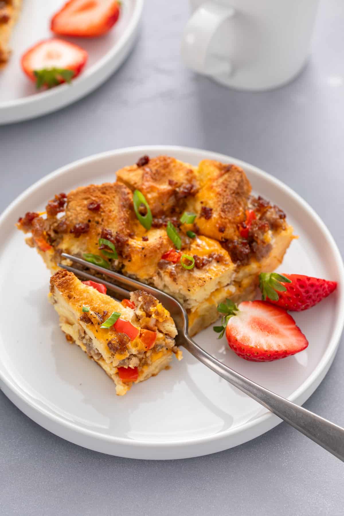 Fork about to take a bite from a slice of make-ahead breakfast casserole on a white plate.