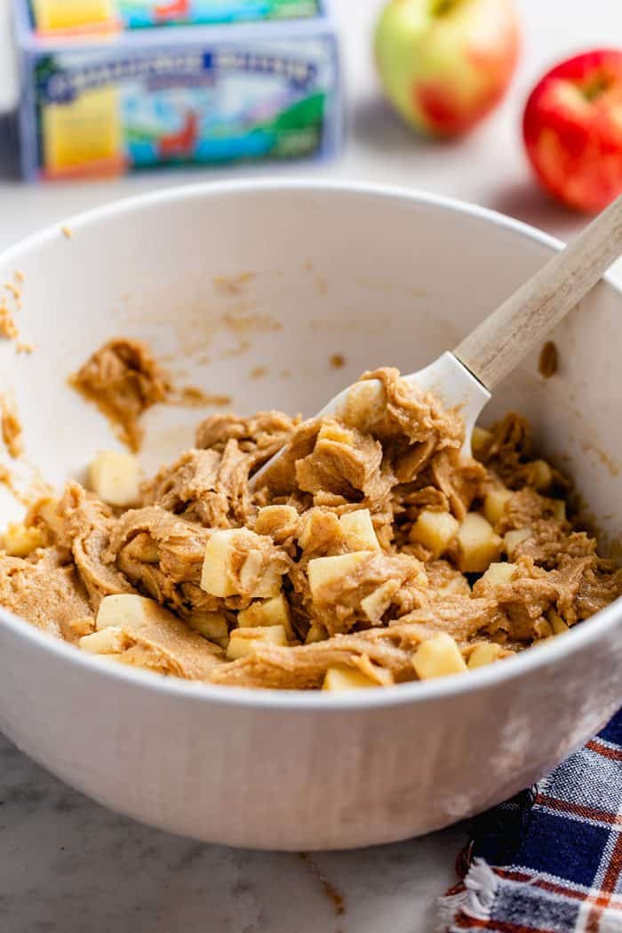 Spatula stirring together apple bar batter in a white bowl