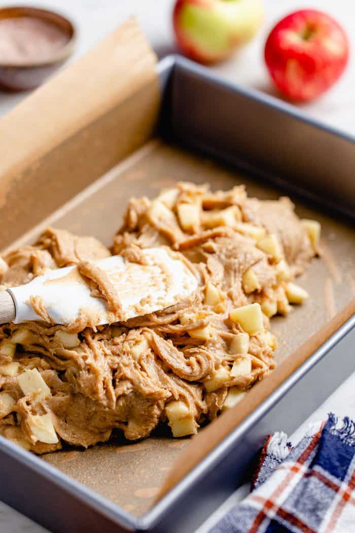 Spatula pressing apple bar batter into a parchment-lined baking pan