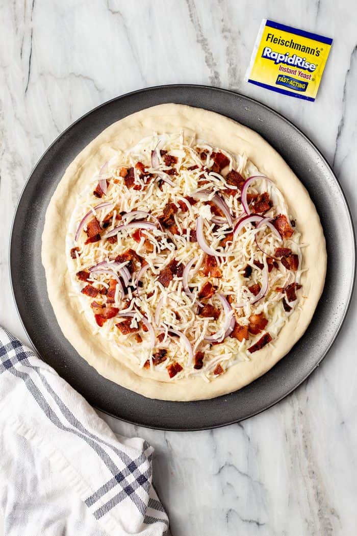 Overhead view of unbaked chicken bacon ranch pizza on a pan, ready to go in the oven