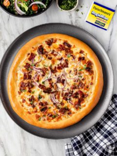 Overhead shot of baked chicken bacon ranch pizza on a platter next to a plaid napkin