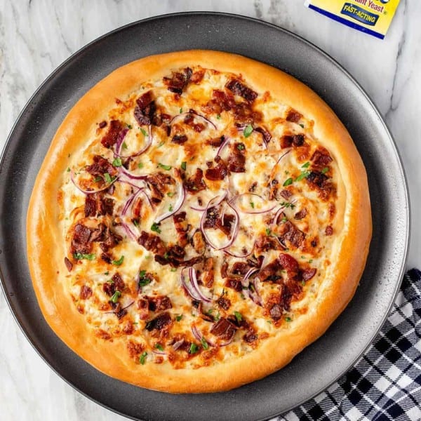 Overhead shot of baked chicken bacon ranch pizza on a platter next to a plaid napkin