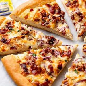 Slices of chicken bacon ranch pizza arranged on a marble surface with a package of yeast in the background