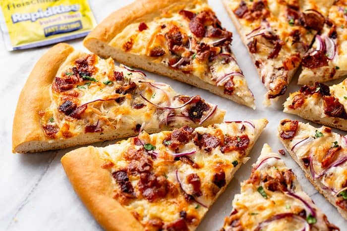 Slices of chicken bacon ranch pizza arranged on a marble surface with a package of yeast in the background