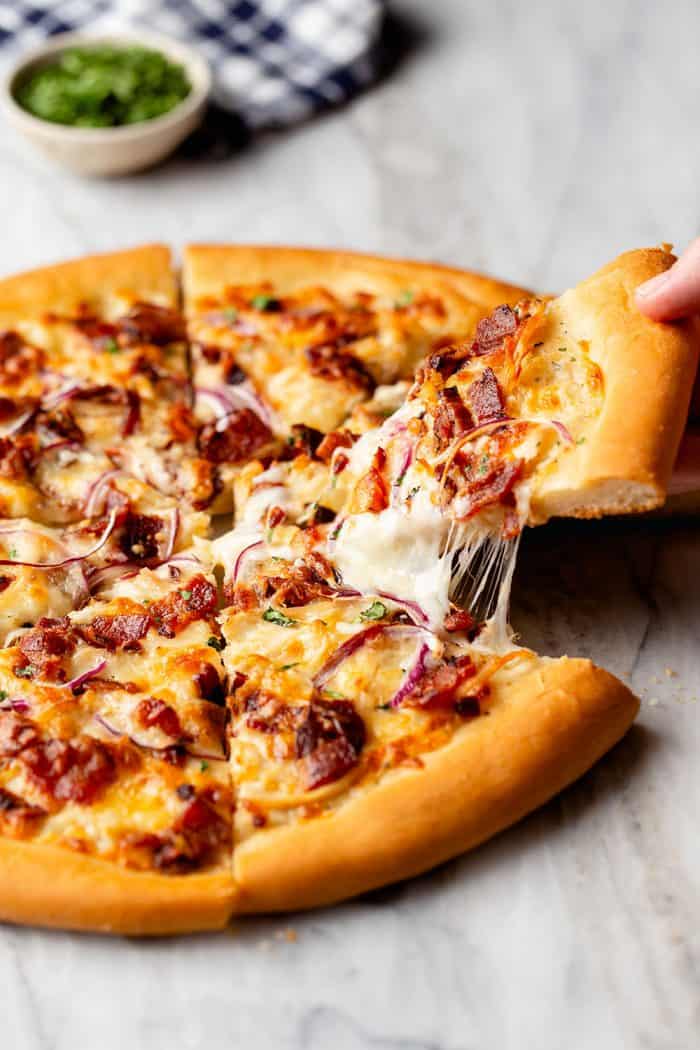 Hand pulling a slice of chicken bacon ranch pizza up, with cheese pulling at the edges