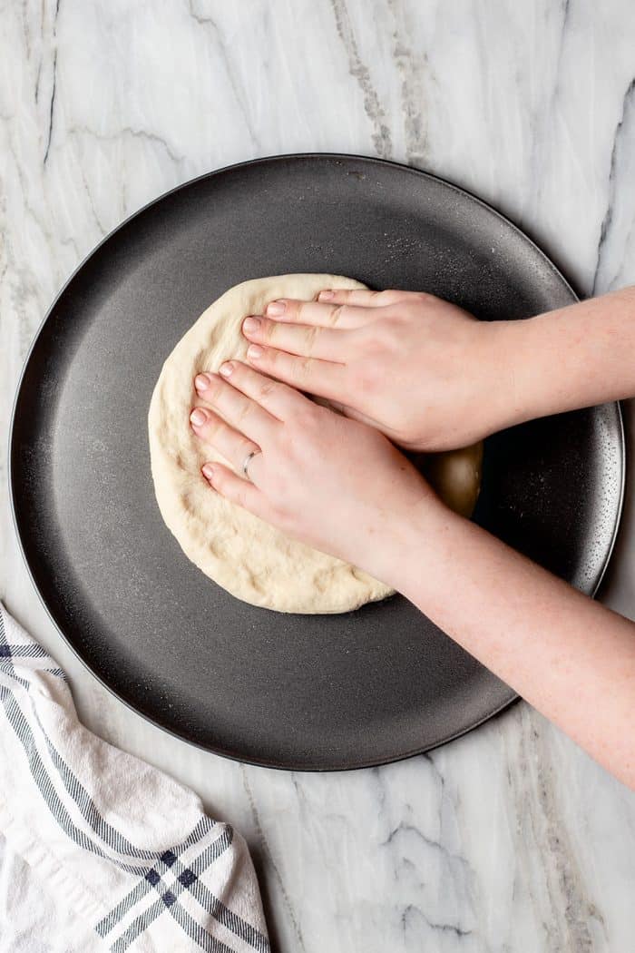 Hand pressing pizza dough into a pan on a marble surface