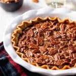 Baked chocolate pecan pie in a white pie plate on top of a plaid towel