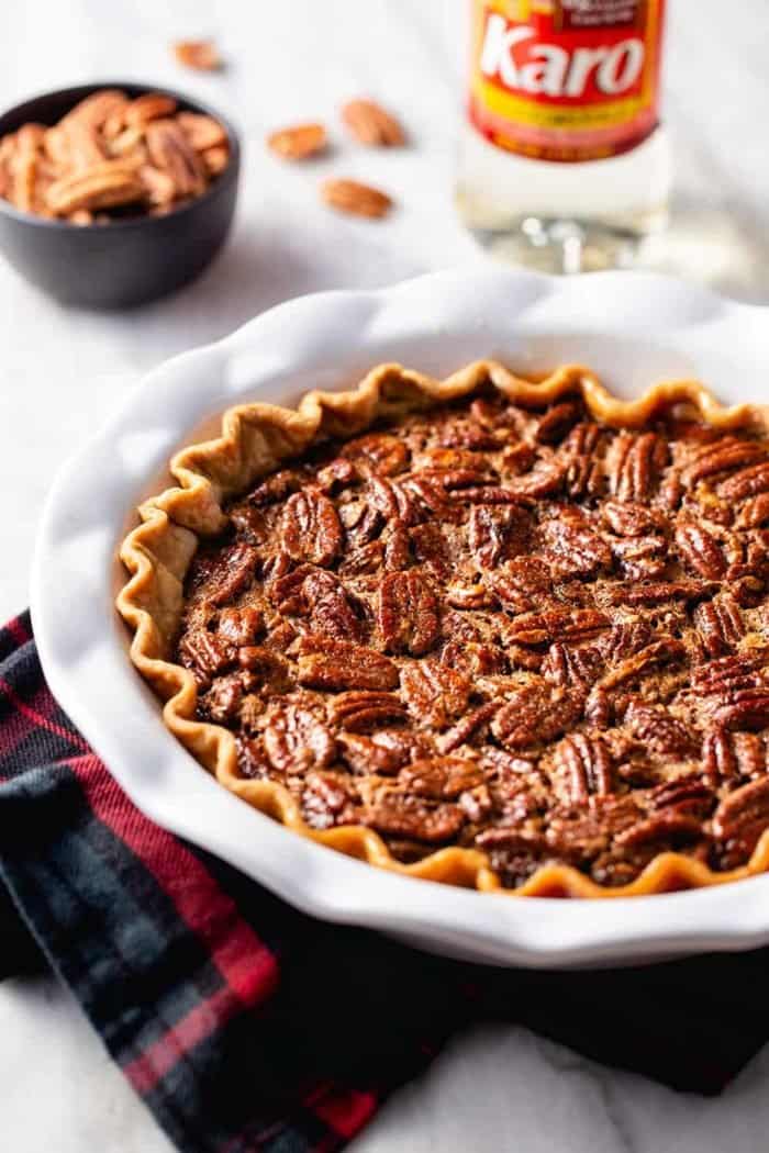 Baked chocolate pecan pie in a white pie plate on top of a plaid towel
