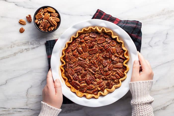 Overhead view of hands setting a chocolate pecan pie on a plaid towel on a marble counter