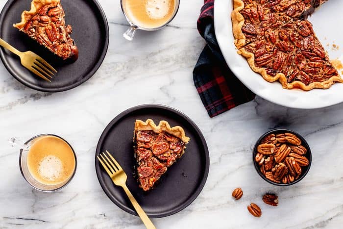 Overhead view of slices of chocolate pecan pie on black plates next to a pie plate of pie