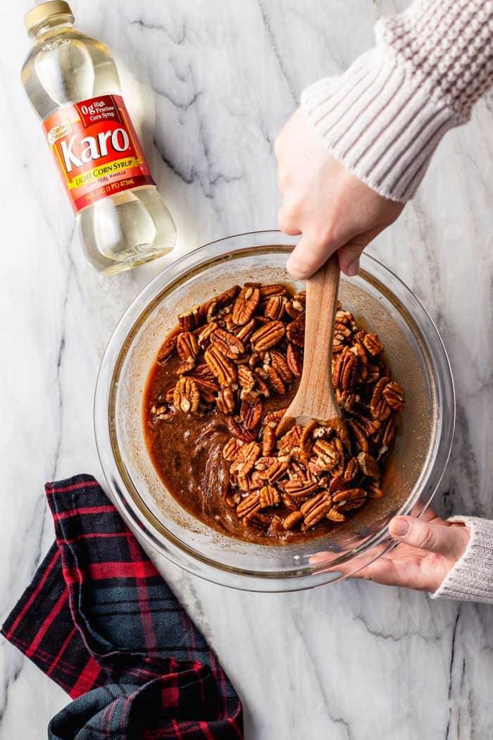 Hands stirring together the filling for chocolate pecan pie in a glass bowl