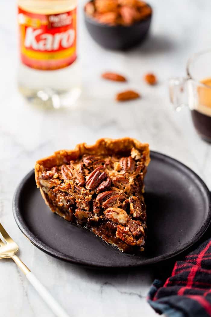Slice of chocolate pecan pie on a black plate with pie ingredients in the background