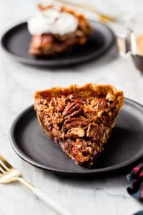 Slice of chocolate pecan pie on a black plate on a marble counter