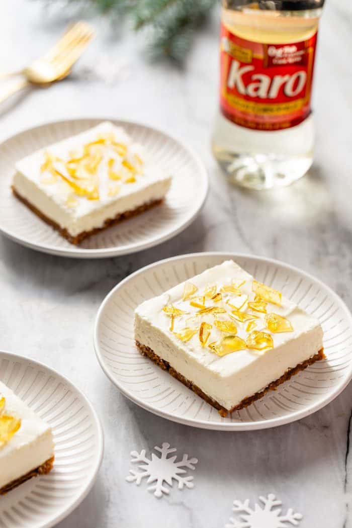 Two white plates with slices of no-bake cheesecake bars topped with cracked sugar. A bottle of corn syrup is in the background