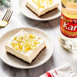 No-bake cheesecake bar on a white plate with a second bar and a bottle of corn syrup in the background