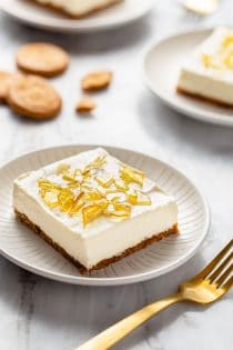 No-bake cheesecake bar with cracked sugar topping on a white plate next to a gold fork