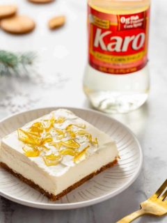 No-bake cheesecake bar with cracked sugar topping on a white plate with a bottle of corn syrup in the background