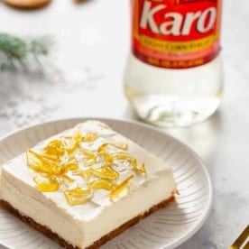 No-bake cheesecake bar with cracked sugar topping on a white plate with a bottle of corn syrup in the background