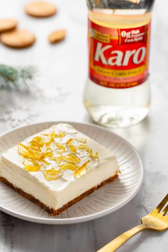 No-bake cheesecake bar with cracked sugar topping on a white plate with a bottle of corn syrup in the background