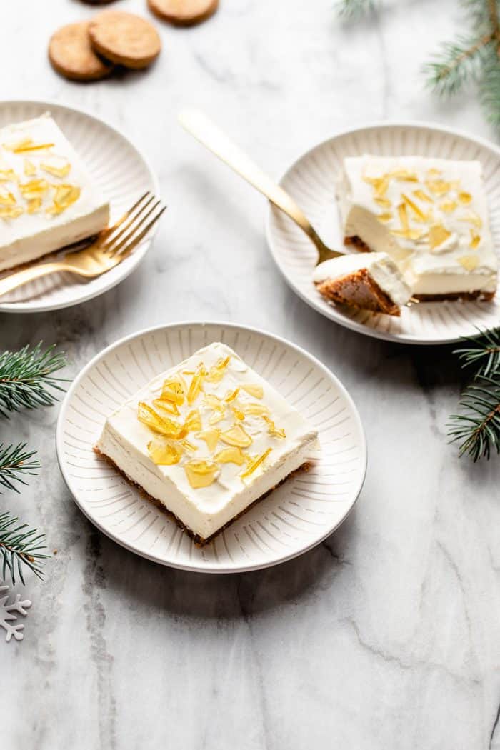 Three white plates each with a slice of no-bake cheesecake bar with sugar topping