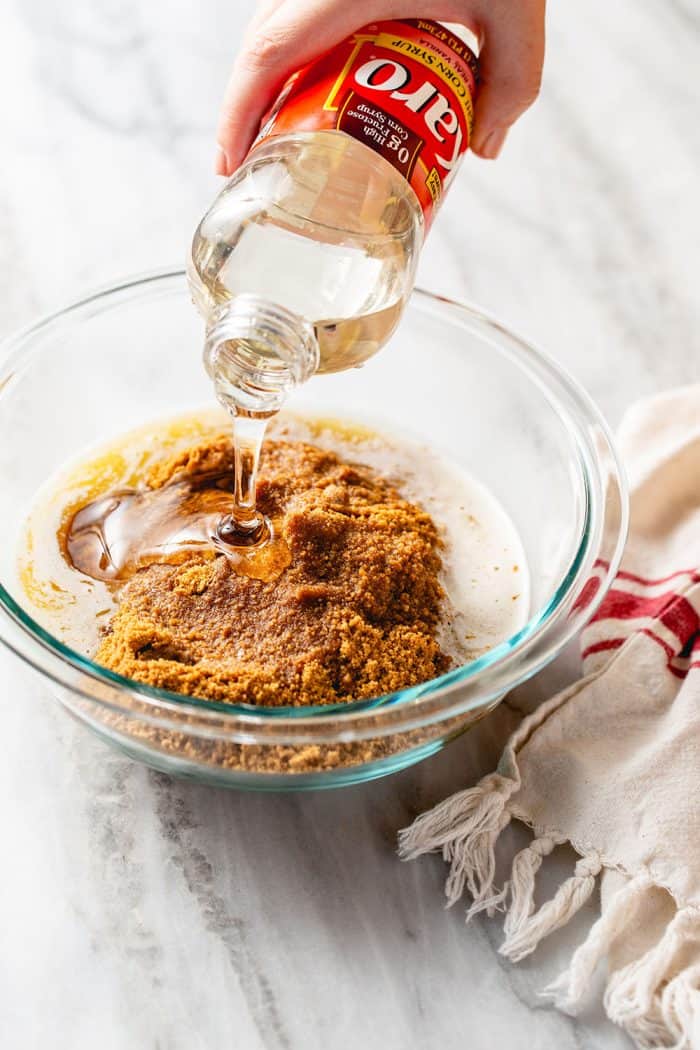 Hand pouring corn syrup into a glass mixing bowl with the ingredients for a cookie crust