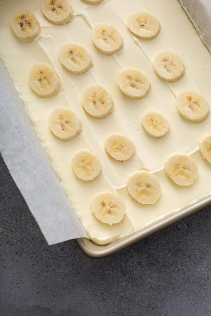 Sliced bananas layered on top of eclair cake filling in a baking pan