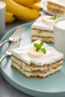 Two slices of banana cream pie eclair cake, a latte and two forks on a blue platter