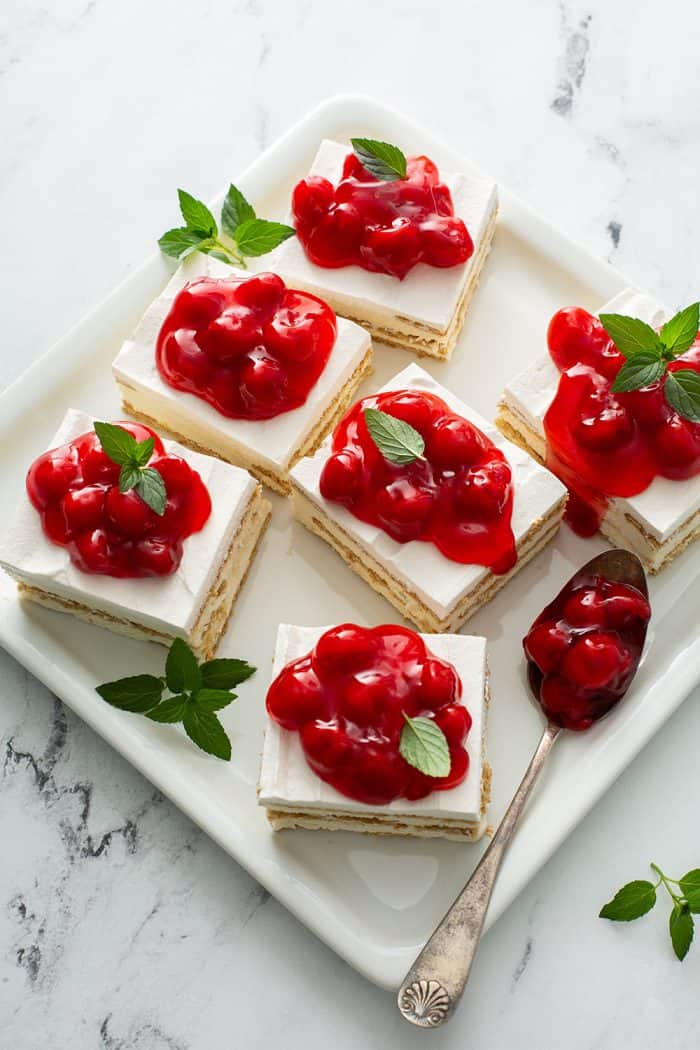 White platter with six slices of cheesecake eclair cake topped with cherry pie filling