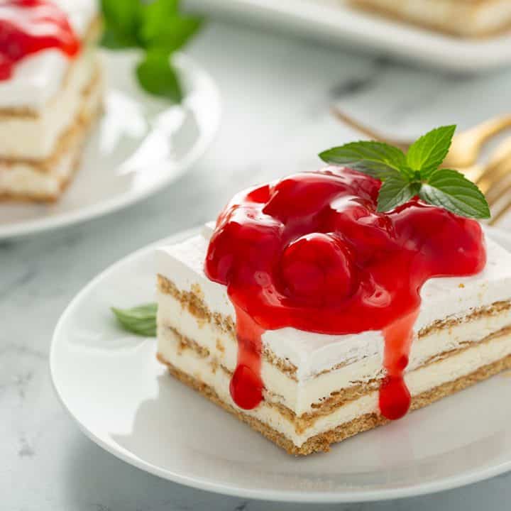 Slice of no-bake cheesecake eclair cake topped with cherry pie filling on a white plate