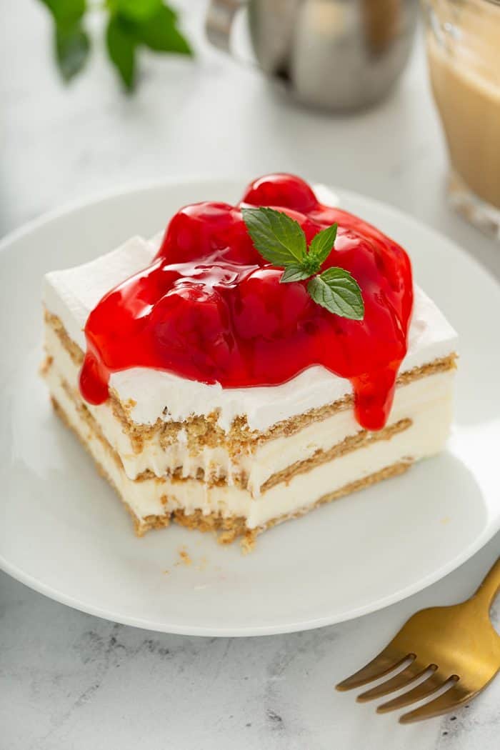 Slice of cheesecake eclair cake on a white plate, with a bite taken out of one corner