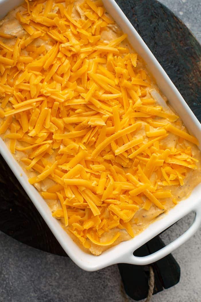 Shredded cheese on top of buffalo chicken dip in a white casserole dish, ready to be baked